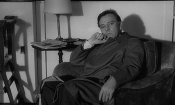 Movie still from “The Spy Who Came in from the Cold” (1965), directed by Martin Ritt – A black and white photo of a man sitting in a chair; Medium shot, Low angle
