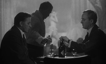 Movie still from “The Spy Who Came in from the Cold” (1965), directed by Martin Ritt – Two men sitting at a table in front of a bottle of wine; Medium shot, Over the shoulder angle