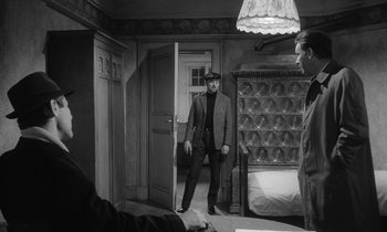 Movie still from “The Spy Who Came in from the Cold” (1965), directed by Martin Ritt – A black and white photo of a man in a suit and hat; Medium shot, Over the shoulder angle