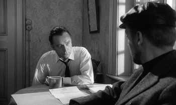 Movie still from “The Spy Who Came in from the Cold” (1965), directed by Martin Ritt – Two men sitting at a table with papers and a cup of coffee; Medium shot, Over the shoulder angle