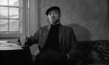 Movie still from “The Spy Who Came in from the Cold” (1965), directed by Martin Ritt – A black and white photo of a man sitting on a couch; Medium shot, Low angle