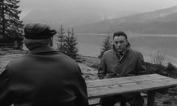 Movie still from “The Spy Who Came in from the Cold” (1965), directed by Martin Ritt – A man sitting at a wooden table in front of another man; Medium shot, Over the shoulder angle