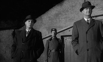 Movie still from “The Spy Who Came in from the Cold” (1965), directed by Martin Ritt – A group of men standing next to each other in front of a building; Medium shot, Low angle