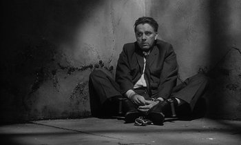 Movie still from “The Spy Who Came in from the Cold” (1965), directed by Martin Ritt – Black and white photograph of a man sitting on the ground; Medium shot, High angle