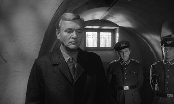 Movie still from “The Spy Who Came in from the Cold” (1965), directed by Martin Ritt – A man and a man in a uniform stand in front of a window; Medium shot, Low angle