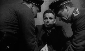 Movie still from “The Spy Who Came in from the Cold” (1965), directed by Martin Ritt – A man in a suit and tie with two other men in uniform; Medium shot, Low angle