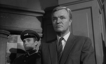 Movie still from “The Spy Who Came in from the Cold” (1965), directed by Martin Ritt – An older man in a suit stands next to a young man in a uniform; Close Up shot, Low angle