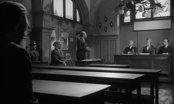 Movie still from “The Spy Who Came in from the Cold” (1965), directed by Martin Ritt – Three men are sitting at a table in a courtroom; Wide shot, High angle