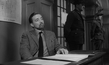 Movie still from “The Spy Who Came in from the Cold” (1965), directed by Martin Ritt – A man sitting at a table in front of another man standing behind him; Medium shot, Low angle