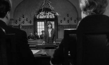 Movie still from “The Spy Who Came in from the Cold” (1965), directed by Martin Ritt – A woman standing in front of a group of people in a courtroom; Wide shot, High angle