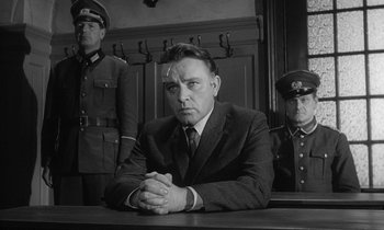 Movie still from “The Spy Who Came in from the Cold” (1965), directed by Martin Ritt – A man sitting in front of two other men in uniform; Medium shot, Low angle