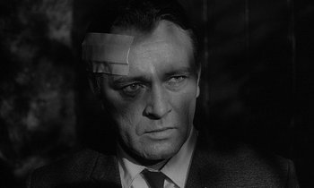 Movie still from “The Spy Who Came in from the Cold” (1965), directed by Martin Ritt – A black and white photo of a man with a bandage on his forehead; Close Up shot, Over the shoulder angle