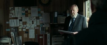 Movie still from “The Square” (2008), directed by Nash Edgerton – An older man in a suit and tie holding papers; Medium shot, Over the shoulder angle