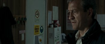 Movie still from “The Square” (2008), directed by Nash Edgerton – A man standing next to a refrigerator in a room; Close Up shot, Over the shoulder angle