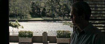 Movie still from “The Square” (2008), directed by Nash Edgerton – A man looking out of a window at a lake; Medium shot, Over the shoulder angle