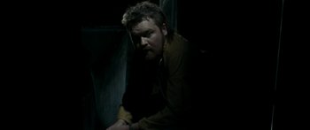 Movie still from “The Square” (2008), directed by Nash Edgerton – A man sitting in a dark room with his head turned to the side; Medium shot, High angle