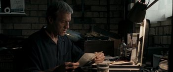 Movie still from “The Square” (2008), directed by Nash Edgerton – A man sitting at a table reading a book; Medium shot, Low angle