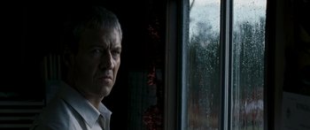 Movie still from “The Square” (2008), directed by Nash Edgerton – A man standing in front of a window looking at the camera; Close Up shot, Low angle