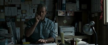 Movie still from “The Square” (2008), directed by Nash Edgerton – A man sitting at a desk talking on a phone; Medium shot, High angle