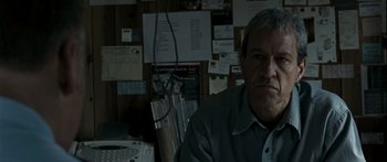 Movie still from “The Square” (2008), directed by Nash Edgerton – A man sitting in front of a wall with papers on the wall behind him; Close Up shot, Low angle