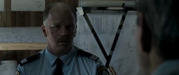 Movie still from “The Square” (2008), directed by Nash Edgerton – A man in a police uniform standing in front of papers; Close Up shot, Over the shoulder angle