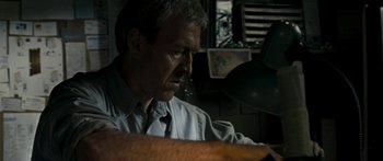 Movie still from “The Square” (2008), directed by Nash Edgerton – A man sitting at a desk looking down at a lamp; Close Up shot, Low angle