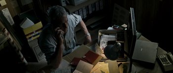 Movie still from “The Square” (2008), directed by Nash Edgerton – An older man sitting at a desk talking on the phone; Medium shot, High angle
