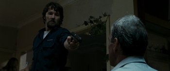 Movie still from “The Square” (2008), directed by Nash Edgerton – A man holding a gun pointed at another man in a room; Medium shot, Over the shoulder angle