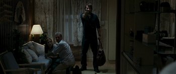 Movie still from “The Square” (2008), directed by Nash Edgerton – A man standing in a living room holding a bag; Wide shot, Over the shoulder angle