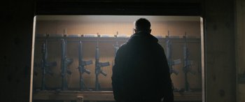 A man standing in front of a wall with guns