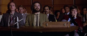 Movie still from “The Star Chamber” (1983), directed by Peter Hyams – A group of people in a courtroom with a man wearing a suit and tie; Medium shot, Low angle