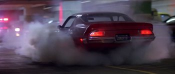 Movie still from “The Star Chamber” (1983), directed by Peter Hyams – A red car is driving down the street with smoke billowing out of the back end; Wide shot, Low angle