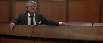 Movie still from “The Star Chamber” (1983), directed by Peter Hyams – A man sitting in front of a wooden table; Medium shot, Low angle