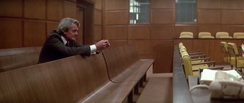 Movie still from “The Star Chamber” (1983), directed by Peter Hyams – A man sitting on a bench in a court room; Medium shot, High angle