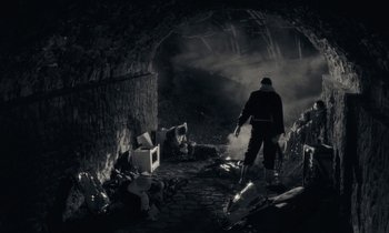 Movie still from “The State of Things” (1982), directed by Wim Wenders – A man is walking through a dark tunnel; Wide shot, High angle