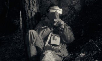 Movie still from “The State of Things” (1982), directed by Wim Wenders – A man sitting on the ground with a box in front of his face; Medium shot, High angle