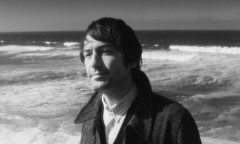 Movie still from “The State of Things” (1982), directed by Wim Wenders – A black and white photo of a man standing in front of the ocean; Close Up shot, High angle