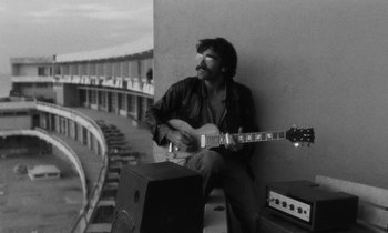 Movie still from “The State of Things” (1982), directed by Wim Wenders – A black and white photo of a man playing a guitar; Medium shot, Low angle