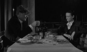 Movie still from “The State of Things” (1982), directed by Wim Wenders – Two people sitting at a dinner table with drinks; Medium shot, Over the shoulder angle
