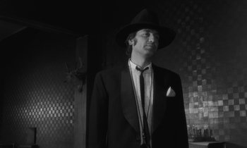 Movie still from “The State of Things” (1982), directed by Wim Wenders – A black and white photo of a man in a suit and hat; Medium shot, Low angle