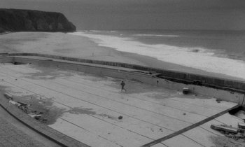 Movie still from “The State of Things” (1982), directed by Wim Wenders – A person standing on the edge of a swimming pool near the ocean; Extreme Wide shot, High angle
