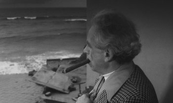 Movie still from “The State of Things” (1982), directed by Wim Wenders – An older man smoking a cigar on the beach; Medium shot, High angle