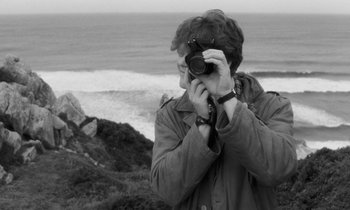 Movie still from “The State of Things” (1982), directed by Wim Wenders – A man taking a picture of the ocean with a camera; Close Up shot, Over the shoulder angle
