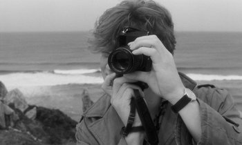 Movie still from “The State of Things” (1982), directed by Wim Wenders – A man taking a picture of the ocean with a camera; Close Up shot, Over the shoulder angle