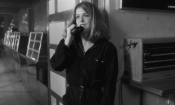 Movie still from “The State of Things” (1982), directed by Wim Wenders – A woman talking on a phone while standing in front of a wall; Medium shot, Low angle