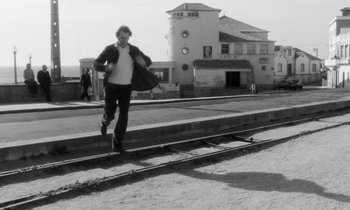 Movie still from “The State of Things” (1982), directed by Wim Wenders – A man walking on a train track in front of a building; Wide shot, Low angle