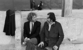 Movie still from “The State of Things” (1982), directed by Wim Wenders – Two men sitting next to each other on steps; Medium shot, High angle