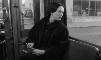Movie still from “The State of Things” (1982), directed by Wim Wenders – A woman sitting on a bench holding a cell phone; Medium shot, Over the shoulder angle