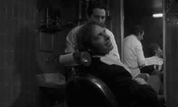 Movie still from “The State of Things” (1982), directed by Wim Wenders – A man sitting in a barber chair while another man looks on; Close Up shot, Over the shoulder angle