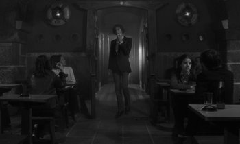 Movie still from “The State of Things” (1982), directed by Wim Wenders – A man standing in a hallway with two other people; Wide shot, Low angle